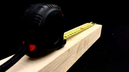 A wooden bar made of fruit wood is measured with a hand tape measure for construction work, the...
