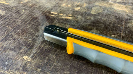 Bright yellow clerical sliding knife with a sharp blade in a carpentry workshop on a table