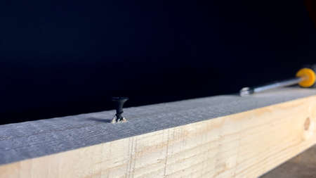 Black self-tapping screws and a screwdriver on an old workshop table. A self-tapping screw is...