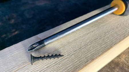 Black self-tapping screws and a screwdriver on an old workshop table. A self-tapping screw is...