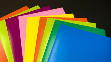 Multi-colored sheets of paper and cardboard are scattered on a black table