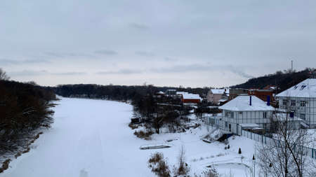 Winter landscape of trees without leaves, a frozen river under a dark sky bridge and a lot of snow