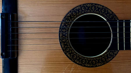 Old acoustic guitar made of light wood with metal strings and black painting