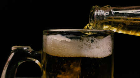 The bartender at the counter pours light beer from a bottle into a mug for a client on a black backgroundの写真素材
