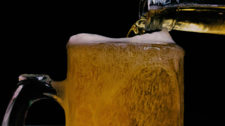 The bartender at the counter pours light beer from a bottle into a mug for a client on a black backgroundの写真素材