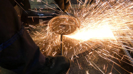 The foreman in the workshop uses a grinder to cut a black steel rebar for the next job in the...