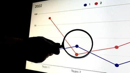 An office worker shows his colleagues a presentation with a company development graph at night on the company's computerの写真素材
