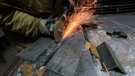 The master of the metal workshop works with the angle grinder in the production of steel parts for...