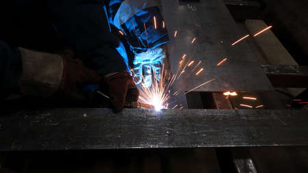 Metal workshop foreman works with welding machine and steel billets