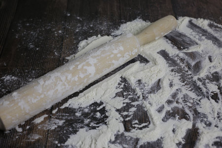 Wooden light rolling pin for dough lies in flour on a dark wooden table. Flour for dough on...