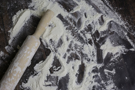 Wooden light rolling pin for dough lies in flour on a dark wooden table. Flour for dough on countertop in kitchenの写真素材