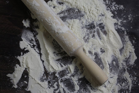 Wooden light rolling pin for dough lies in flour on a dark wooden table. Flour for dough on...