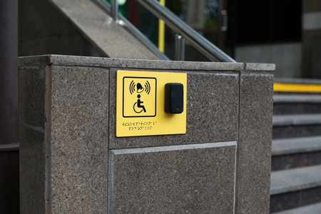 Yellow plate with image of disabled person in wheelchair and call button. Disabled person sign and panic button for help in front of the entrance to the building, brailleの写真素材