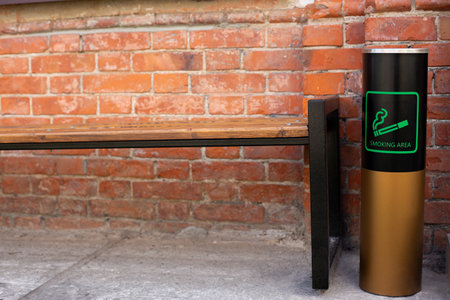 Cylindrical waste bin with a sign indicating a smoking area outside near a bench in a summer cafe on the terraceの写真素材
