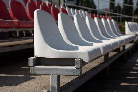 Row of white stained plastic seats for fans on the tribune of an open-air sports stadiumの写真素材