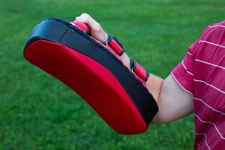 Man's hand holds a red makiwara for punches and kicks against the background of grass in a street training for practicing punches in a fightの写真素材