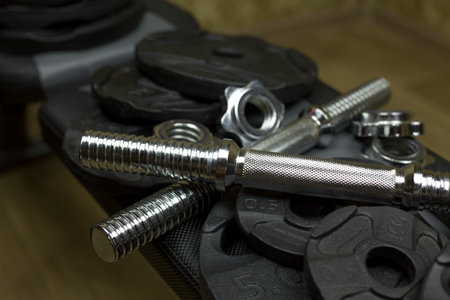 Metal bar for adjustable dumbbells lies on the plates next to the nut for assembling the dumbbell on a sports bench for weightlifting at homeの写真素材