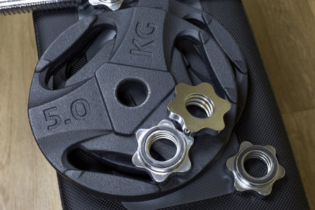 Five-kilogram black dumbbell plates and a barbell next to a screw-on clamp for attaching to a barbell lies on sport benchの写真素材