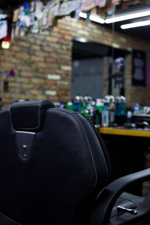Vertical photo of the back of a black leather chair in a barbershop opposite a mirror and a table with barber toolsの写真素材