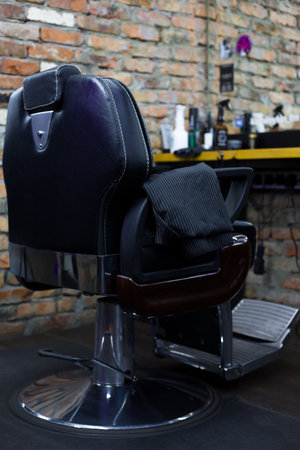 Black leather chair in a barbershop in front of a mirror and a hairdresser's table with hair care accessories, vertical photo back viewの写真素材
