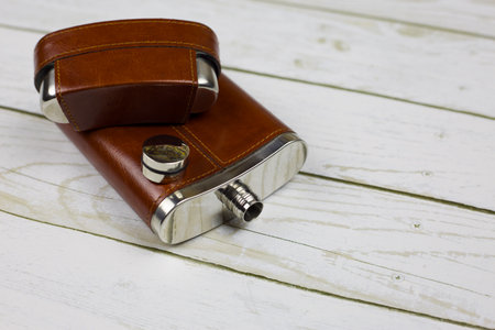An open leather flask for alcohol with leather trim lies on a white wooden tableの写真素材