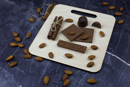 Chocolates on wooden board on dark marble table. Sweet treats made from milk chocolate with almondsの写真素材