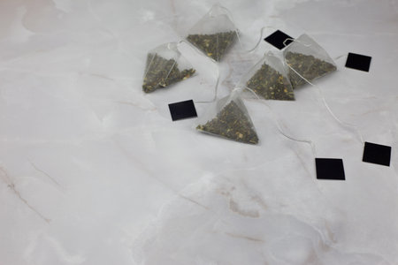 Nylon tea bags lie on a white marble table. Green tea in pyramids for convenient brewing of a homemade drinkの写真素材