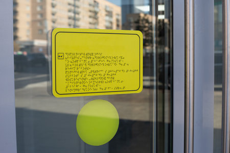 Yellow sign with black writing braille text. The sign is in language for blind people. Means of communication with people with disabilities on sign on door on entrance to the buildingの写真素材