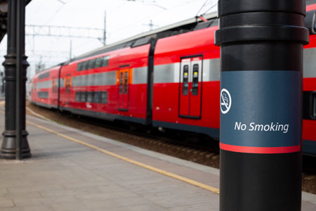 Inscription on pole prohibiting smoking on the platform with passing train in background, no smoking sign on platform, city transport in public placeの写真素材