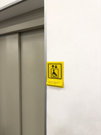 Yellow sign indicating elevator for disabled people in public place. Signboard with braille text at...
