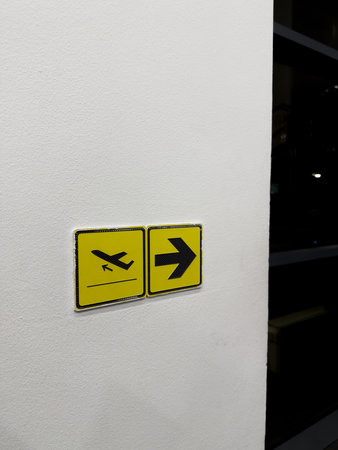 Sign with airplane symbol and arrow on wall indicating direction of departure of aircrafts at international airport. Assistance with orientation at airport, vertical photoの写真素材