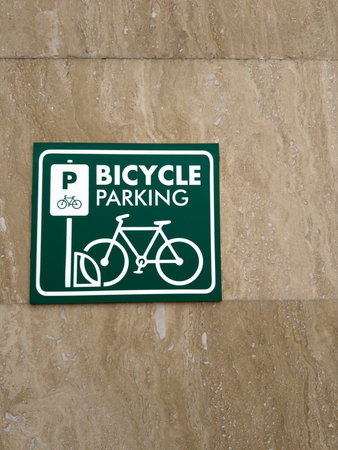 Close up vertical photography of bicycle parking sign on wall to indicate secure bicycle storage area on street in front of building. Bicycle parking icon with green background on wallの写真素材