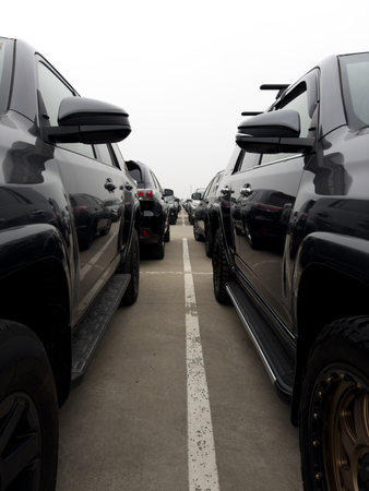 Vertical photo between two black SUVs in street parking lot for new cars. Car market on street with...