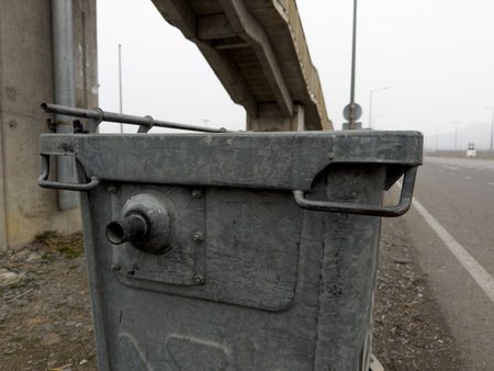 Metal trash can on street along road for waste collection. Steel bin on wheels for collecting garbage. Close up photo of standard trash can bodyの写真素材