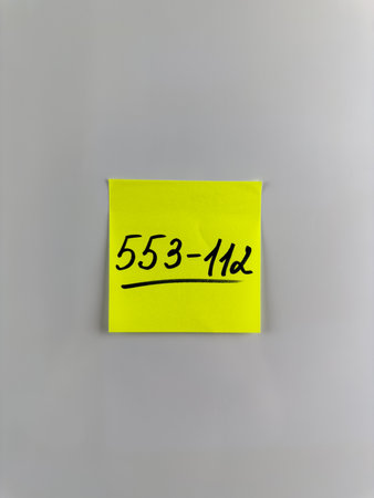 Vertical photo of phone number written on sticky note. Reminder with phone number on white background. Concept of writing phone number on paper. Don't forget to call back the phone numberの写真素材