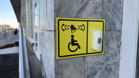 Accessibility assistance button with wheelchair symbol on yellow sign attached to marble wall near...