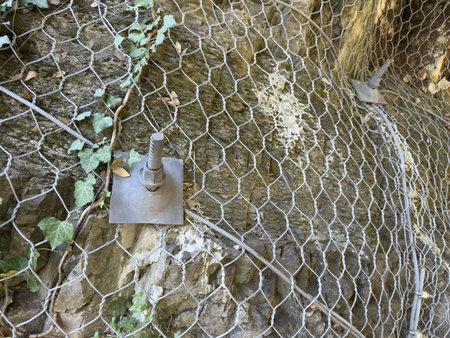 Steel net system fixed with large bolt plate on rocky cliff prevents falling rocks. Vital infrastructure for road safety and environmental protection in unstable mountainous areasの写真素材