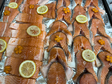 Fresh raw salmon fillets and steaks decorated with lemon slices and carrot flowers, displayed on foil, perfect for cooking or recipe contentの写真素材