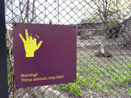 Warning sign on zoo enclosure fence showing bitten hand and message. These animals may bite to caution visitors and promote safety awareness around wild animalsの写真素材