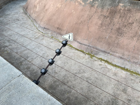 Electric fence with warning symbol showing lightning bolt installed along concrete barrier in...