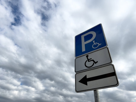 Handicap parking sign with directional arrow on cloudy day, indicating accessible parking for people with disabilities, promoting inclusion and barrier free infrastructureの写真素材