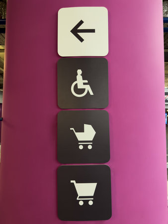 Bright magenta pillar with intuitive white and black signage indicating accessible routes and designated areas for wheelchairs, strollers, and shopping carts in modern retail or parking facilityの写真素材