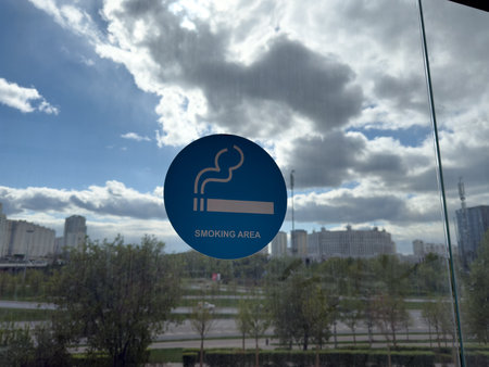 Blue smoking area sign on glass wall with urban view in background, illustrating the widespread normalization of smoking and growing demand for designated spaces in modern public environmentsの写真素材