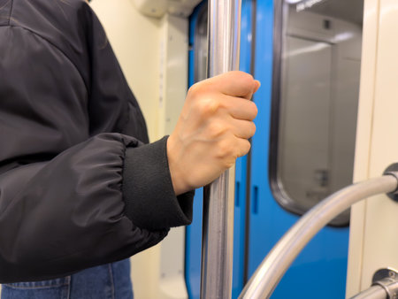 Close up of person holding metal handrail in the metro carriage. Symbolizing stability, safety and urban mobility in everyday public transport commuteの写真素材