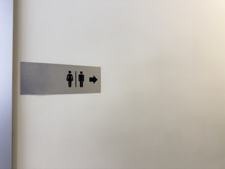 Minimalistic directional toilet sign with male and female symbols and a right arrow on a metallic plate, mounted on a clean white wall in a modern indoor facilityの写真素材