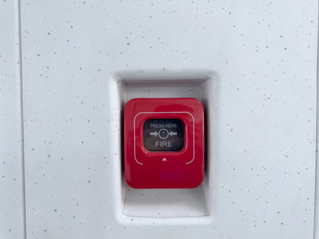 Red fire alarm emergency button mounted on modern speckled wall. Safety equipment detail for use in case of fire, essential in public transportation and commercial buildingsの写真素材