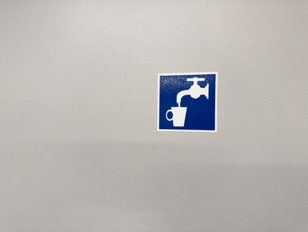 Minimalist white icon on a blue background showing a water tap and cup, representing drinkable water through simple universal visual language and modern signage designの写真素材