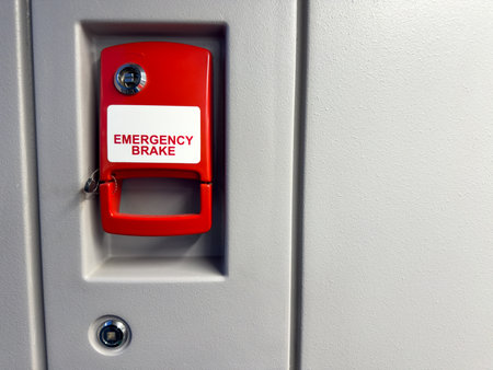 Bright red emergency brake handle mounted on gray wall inside a modern public transport vehicle, designed for quick manual activation in case of urgent situationsの写真素材