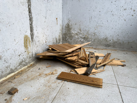 Scattered pile of splintered wooden boards on a tiled floor near stained concrete wall, capturing the aftermath of construction work, material removal or DIY dismantling in an indoor spaceの写真素材