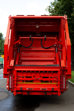 Back view of red garbage truck with hydraulic mechanism, control levers, and metal components....